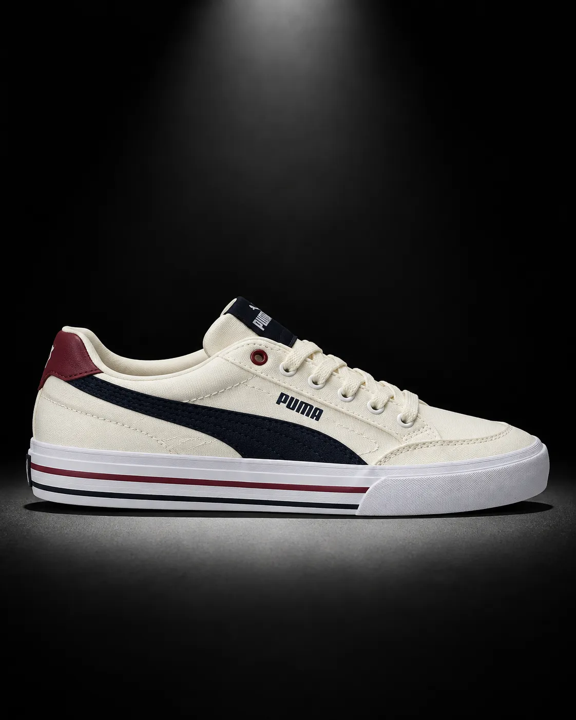 A cream Puma sneaker in full side profile under a single spotlight against a matte black background