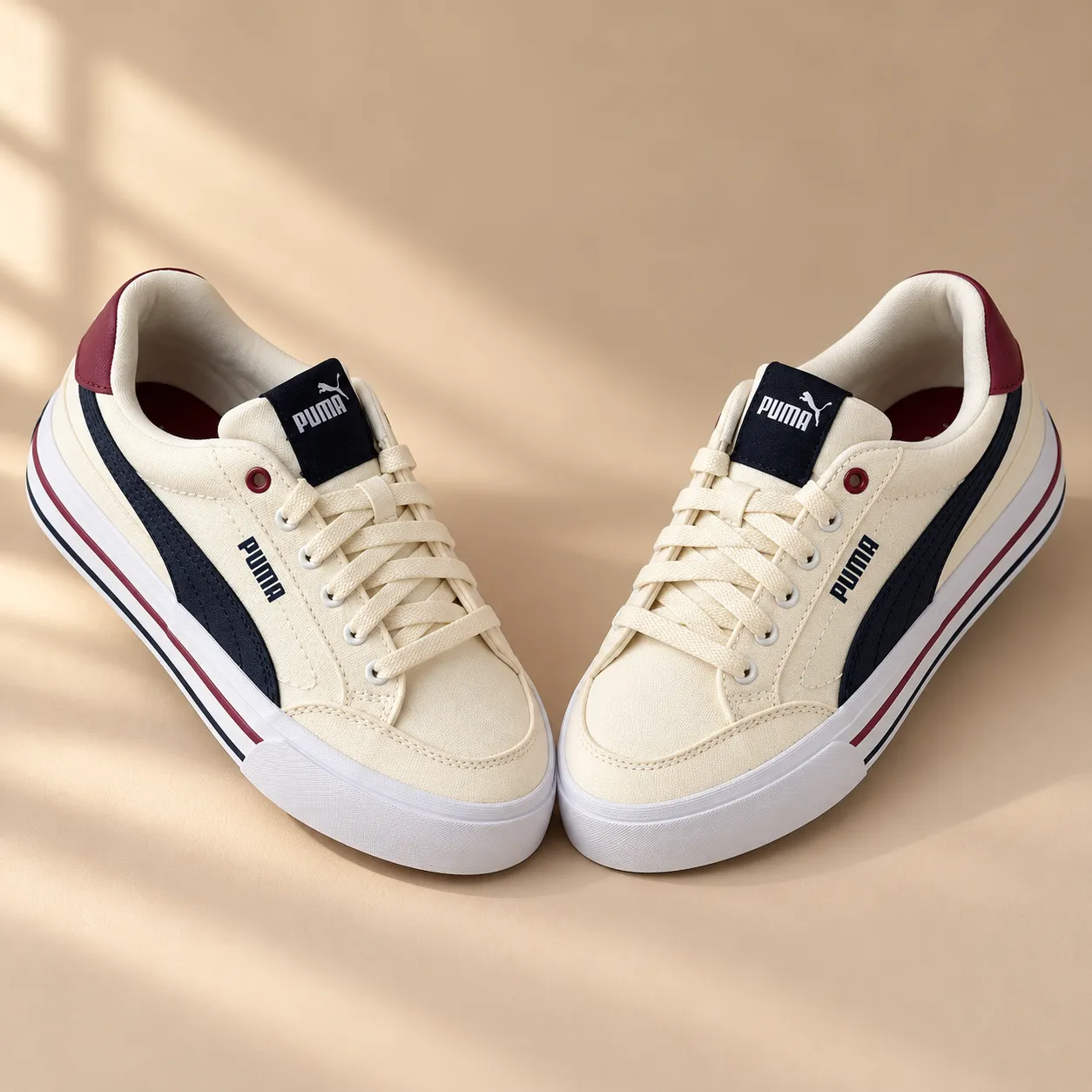 A symmetrical pair of cream Puma sneakers angled toward each other on a warm beige studio surface