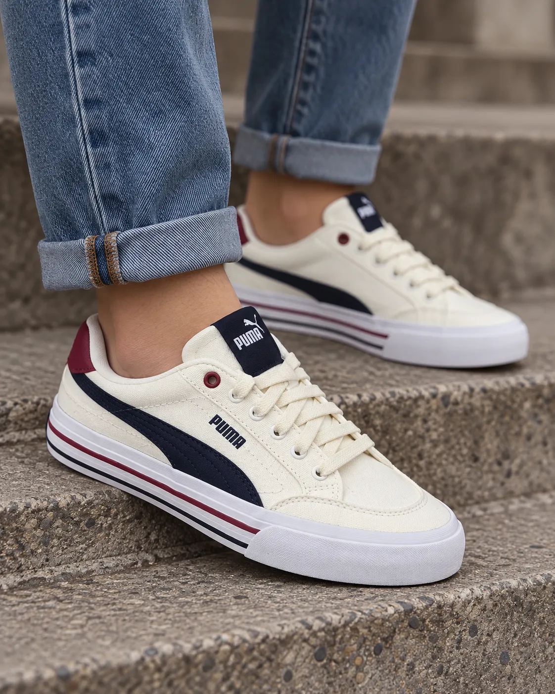 Legs in rolled denim wearing cream Puma sneakers on a concrete step in soft daylight