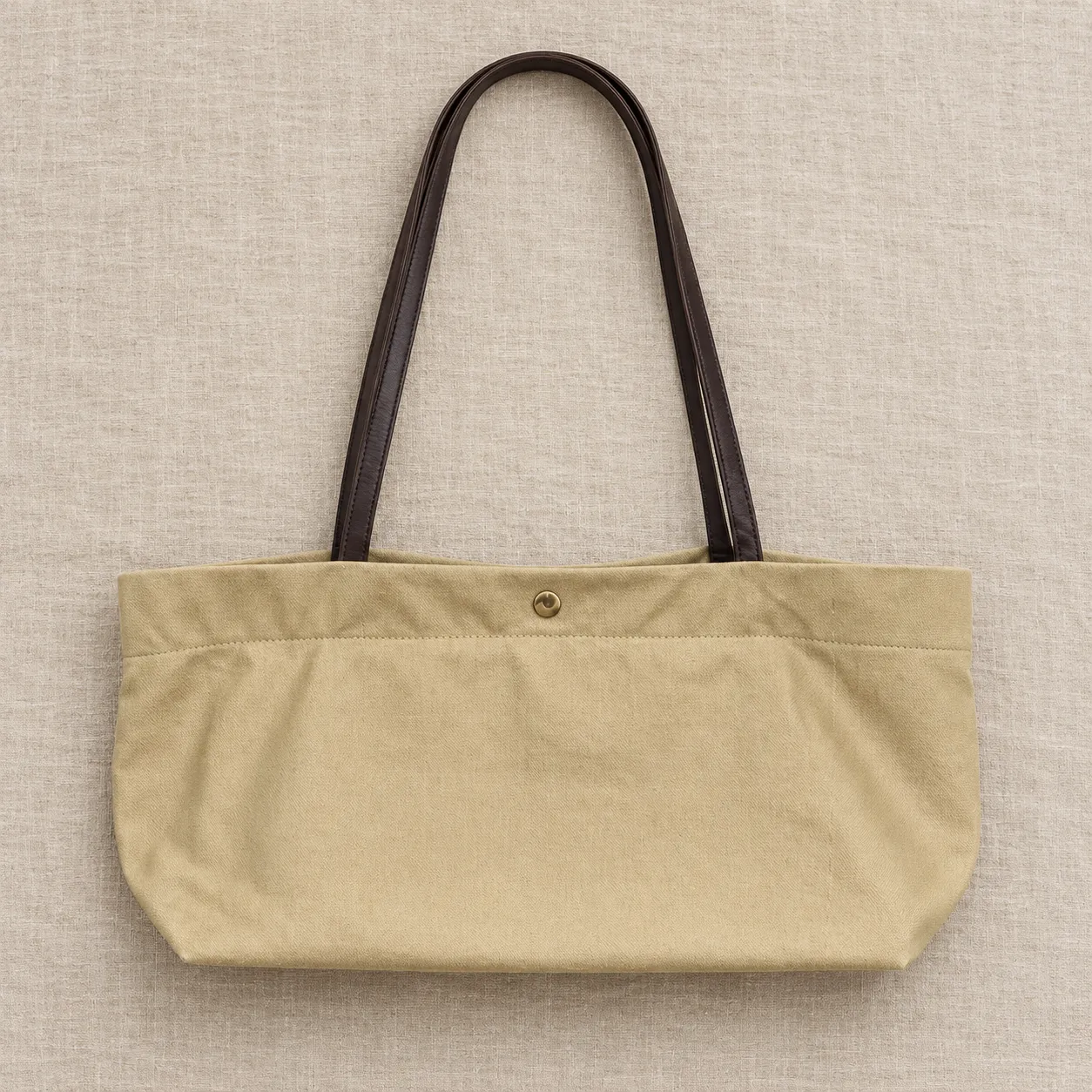 Canvas tote bag laid flat on a neutral linen surface, soft overhead light from a large diffuser, top-down angle, shot on a 35mm lens at f/8, minimal everyday mood, neutral beige color grade, commercial product photography, 1:1.