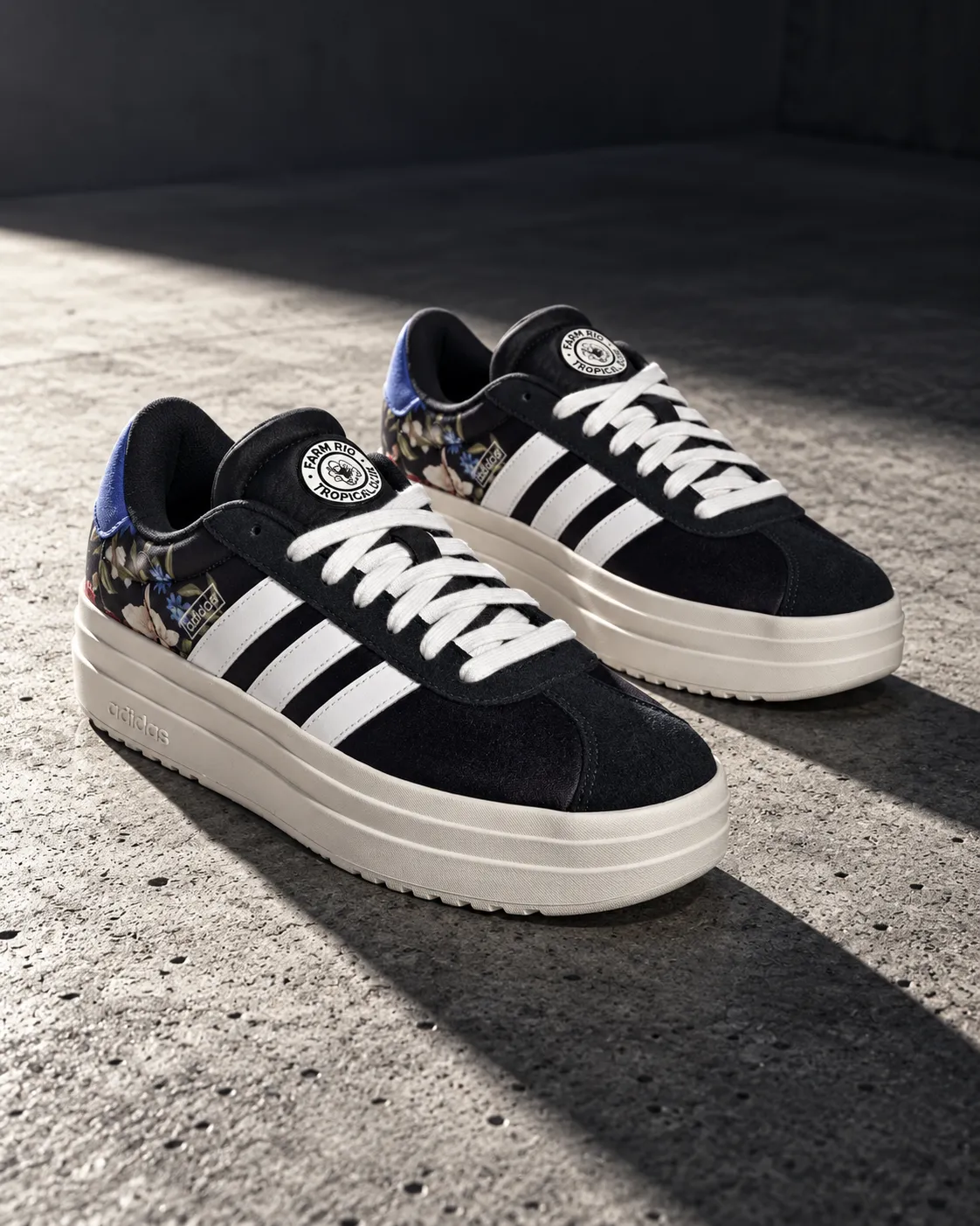 Pair of sneakers on a concrete surface with hard directional light from a single spotlight casting a long shadow, low-angle shot, shot on a 35mm lens at f/4, bold streetwear mood, high-contrast cool gray color grade, commercial product photography, 4:5.